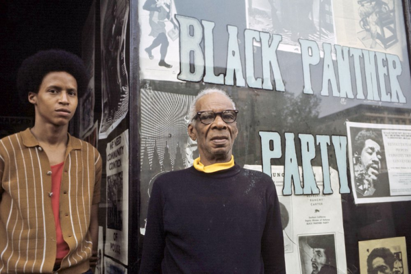 Black Panther Party members stand in front of flyers of imprisoned party members
