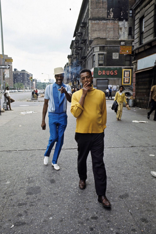 Harlem: The Ghetto. New York City- Harlem- juillet 1970: le ghetto; un homme afro-amÈricain fume en marchant dans une rue, pointÈ du doigt en arriËre par un compatriote en costume bleu et chapeau. (Photo by Jack Garofalo/Paris Match via Getty Images)